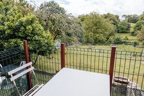Un espace extérieur clos, aménagé avec une table et des chaises, et entouré de verdure et d’arbres.
