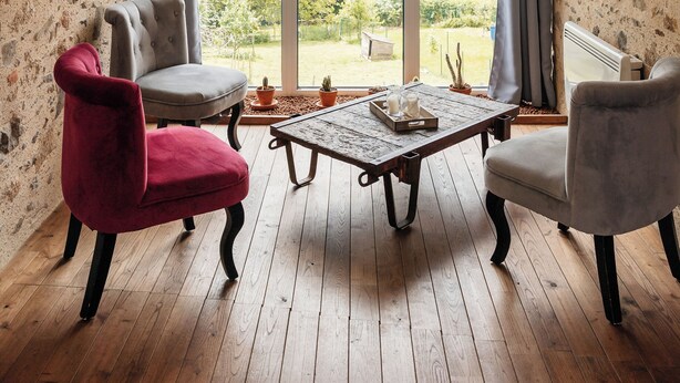 A room with a stone wall, a wooden floor, a red chair, a grey chair, and a table with a tray. - Cottage 7 people near Puy du Fou (Sèvremont)