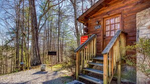 Une cabane en bois avec un mur en pierre, portant le numéro 3083, et un paillasson à l’entrée.