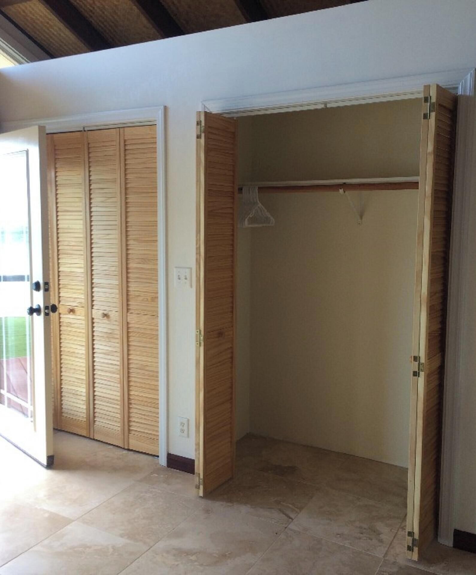 A room with a wooden closet and a hanging rod, tiled floor, and a window with blinds.