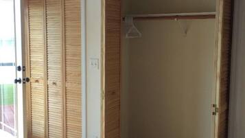 A room with a wooden closet and a hanging rod, tiled floor, and a window with blinds.