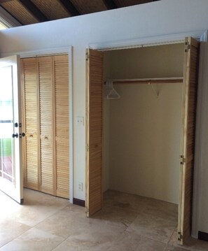 Une pièce avec une armoire en bois et une tringle à vêtements, un sol carrelé et une fenêtre avec des stores.