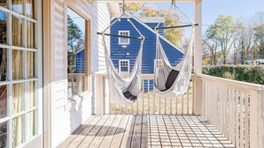 A porch with a hammock swing, a wooden deck, and a blue house in the background. - Spacious Open-Concept Durham Home (Durham)