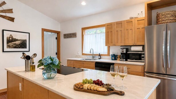 A modern kitchen with wooden cabinets, a stainless steel refrigerator, a marble countertop, and a central island with food and drinks. - Spacious Open-Concept Durham Home (Durham)