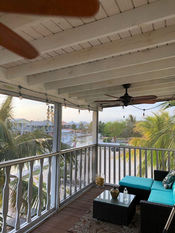 A covered balcony with a ceiling fan, a view of a waterway, and outdoor seating.