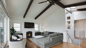 Un salón amplio con chimenea, un sofá seccional gris grande, un sillón blanco y una mesa de centro.