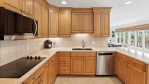 A modern kitchen with wooden cabinets, a stainless steel microwave, a built-in oven, a dishwasher, and a large window offering a view of the outdoors.