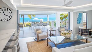 A modern living room with a large clock, a glass coffee table, and a view of the ocean.