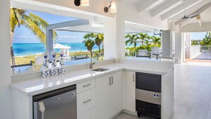 A modern kitchen with white cabinetry, a stainless steel dishwasher, and a view of the ocean.