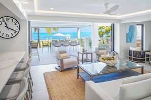 Un salon moderne avec une grande horloge, une table basse en verre et une vue sur l’océan.