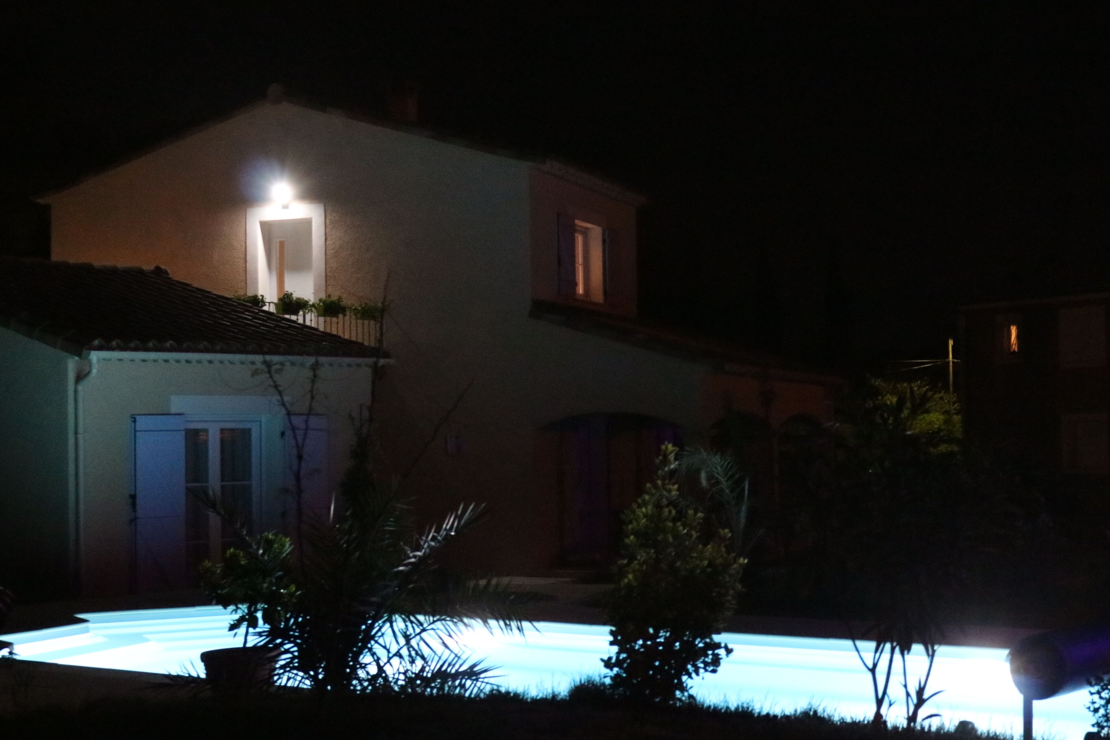 Une maison avec une piscine, illuminée par une seule source de lumière, la nuit.