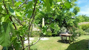 Een goed onderhouden tuin met een houten tafel en stoelen, omringd door weelderige begroeiing en een heldere lucht.