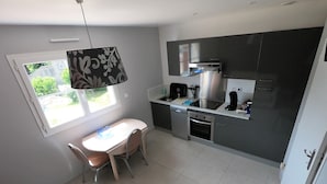 Een kleine keuken met een eettafel, stoelen, een inbouwoven en een raam met uitzicht op groen.