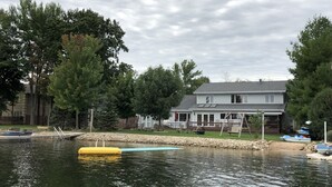 Een huis aan het meer met een steiger, omringd door bomen en een zandstrand.