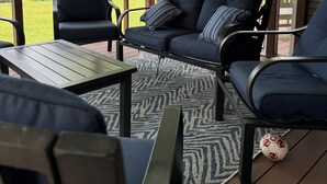 Een overdekt terras met uitzicht op een meer, met een bank, stoelen en een tafel.