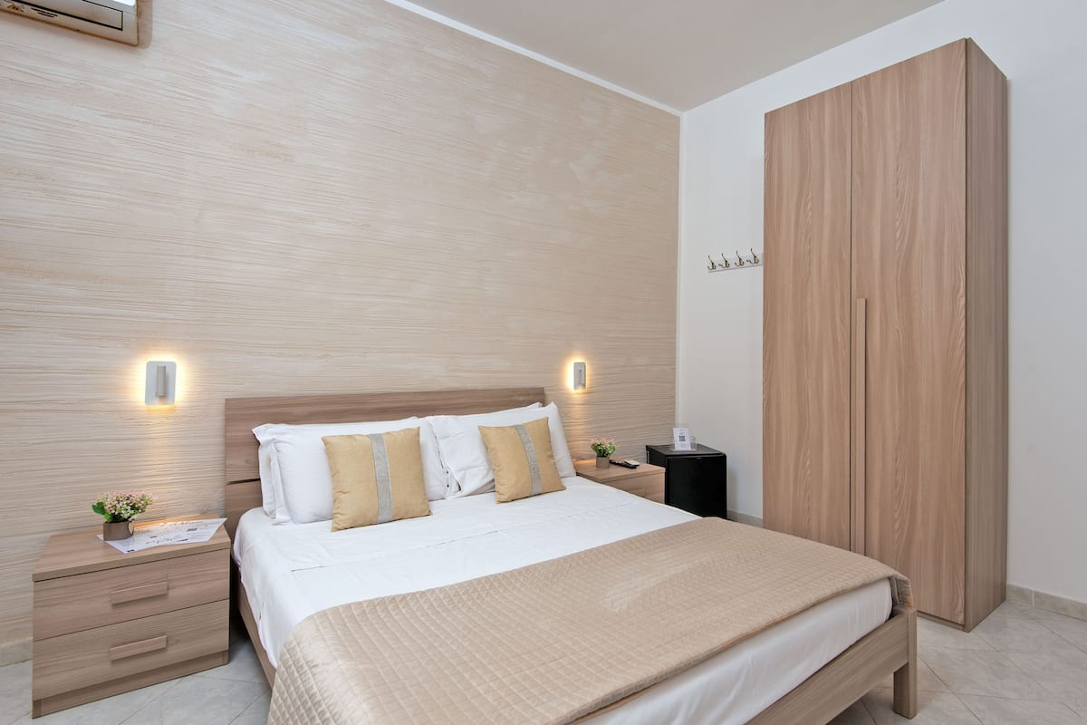 A neatly arranged bedroom with a wooden headboard, a large wardrobe, and bedside tables with lamps.