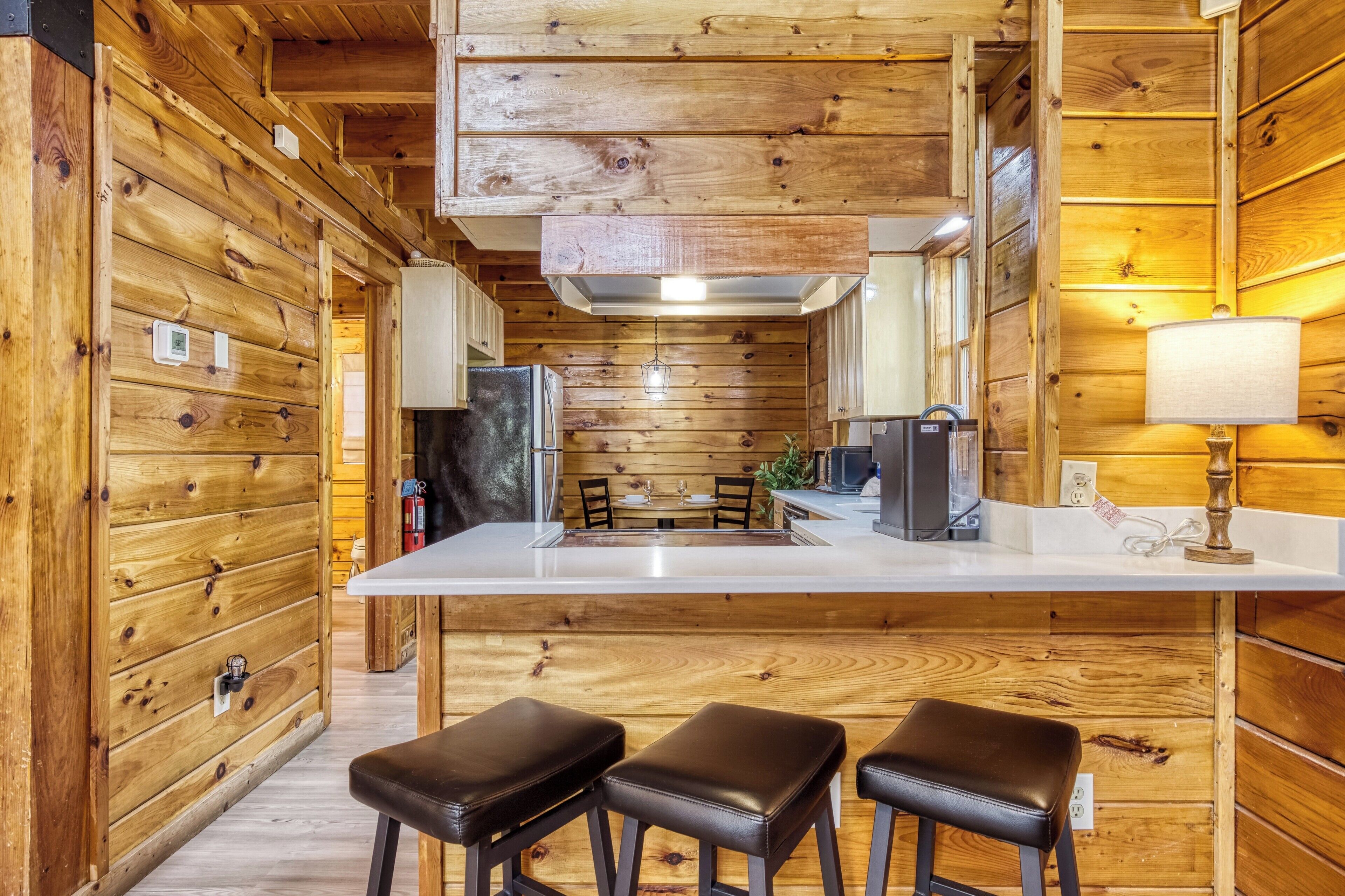 A wooden interior with a kitchen area, bar stools, and a dining table.