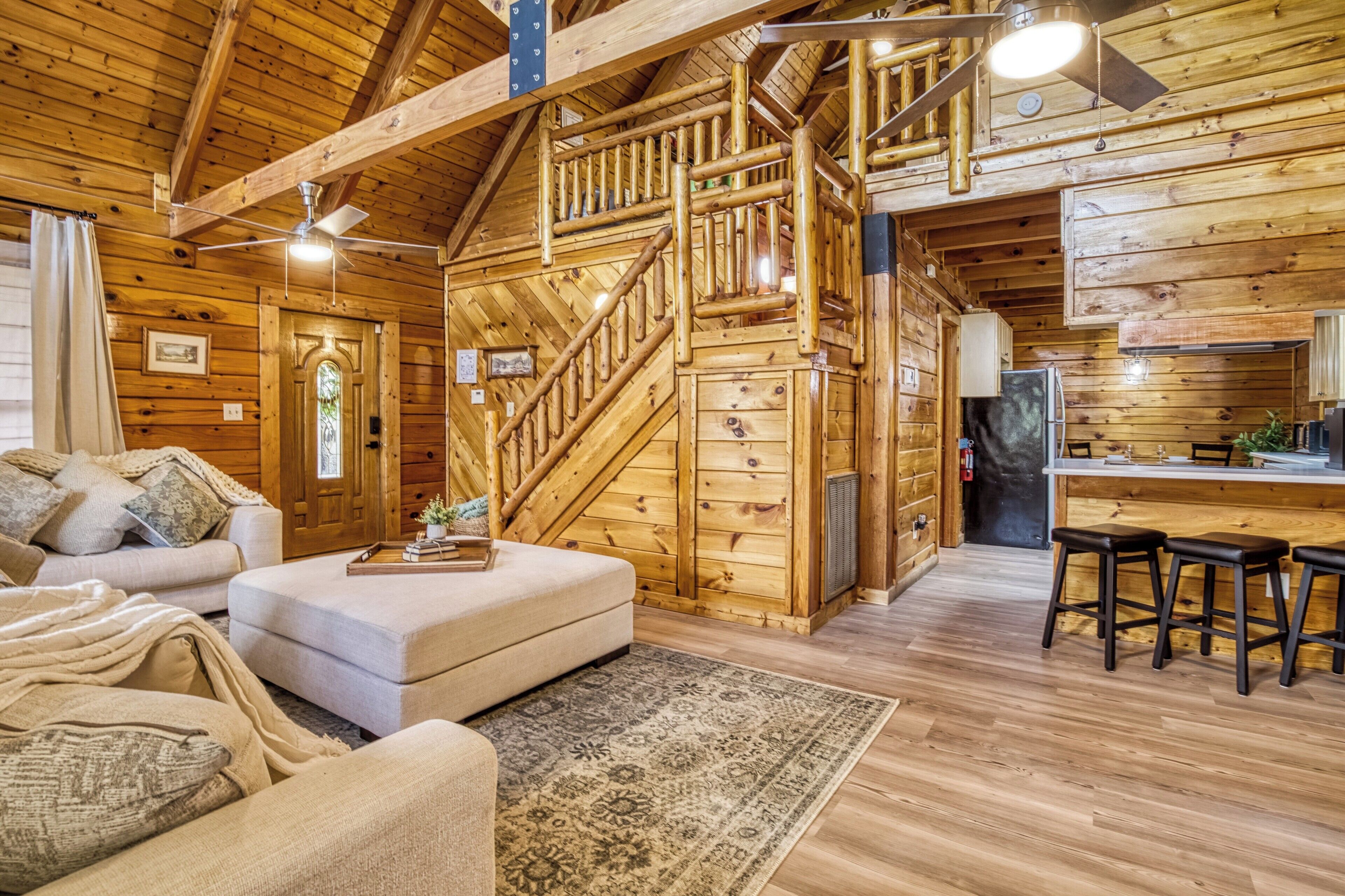 A log cabin interior with a staircase, a sofa, a coffee table, and a kitchen area.