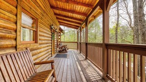 Una cabaña de madera con un porche, bancos de madera y vistas a árboles.