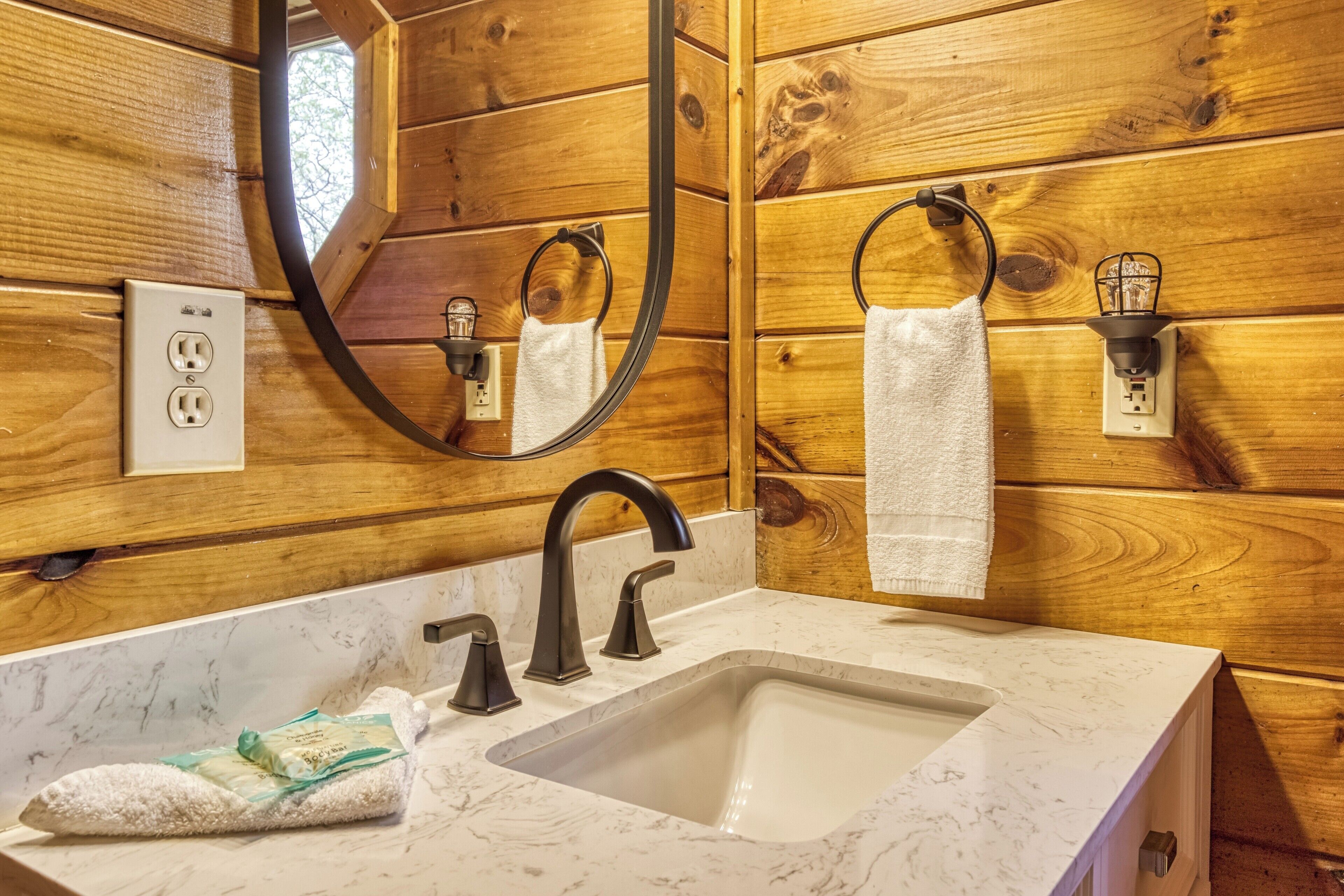 A wooden cabin-style bathroom with a marble sink, black faucets, a mirror, and a towel ring.