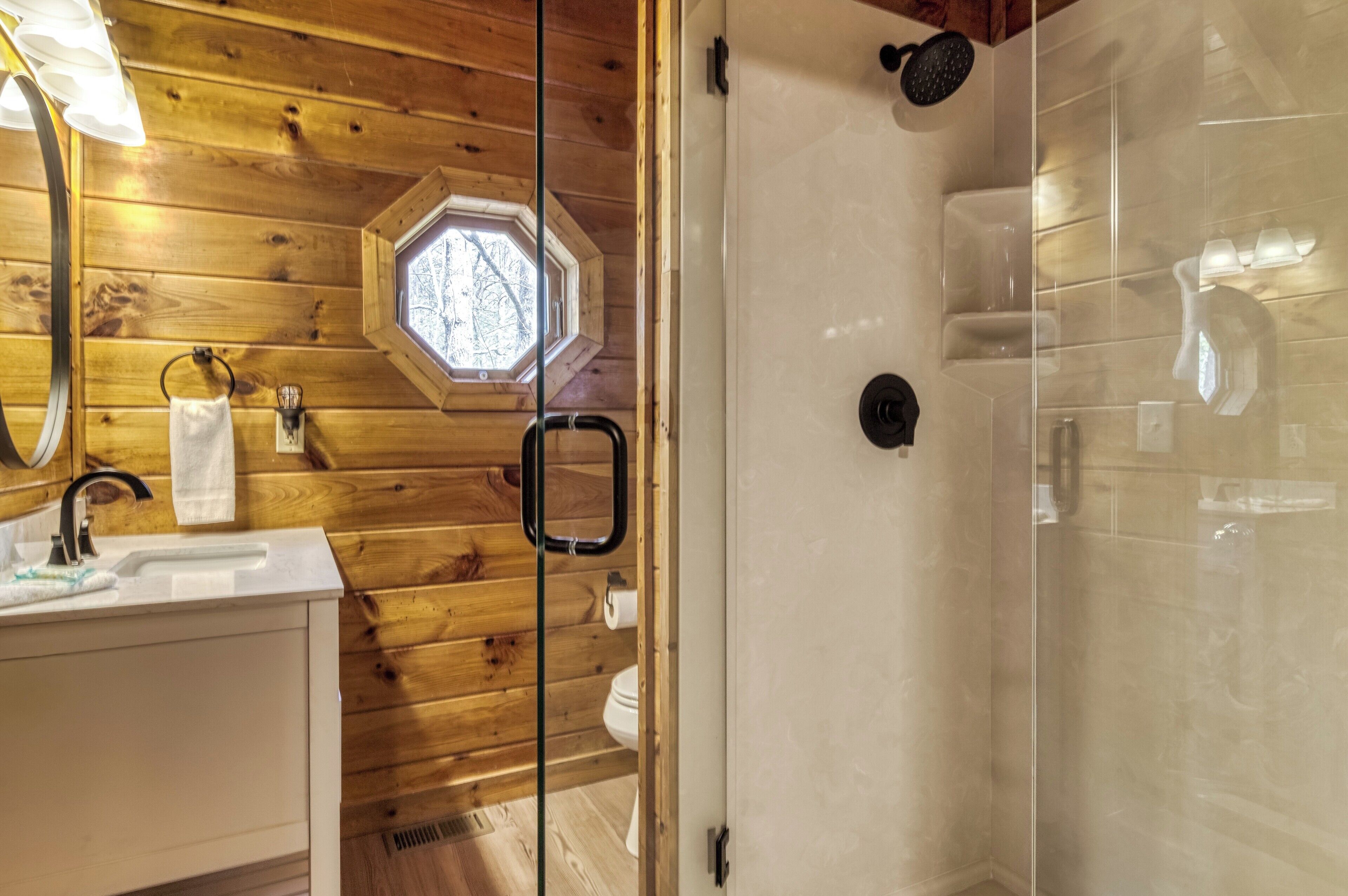 A wooden interior with a glass shower enclosure, a sink, and a window with a view.