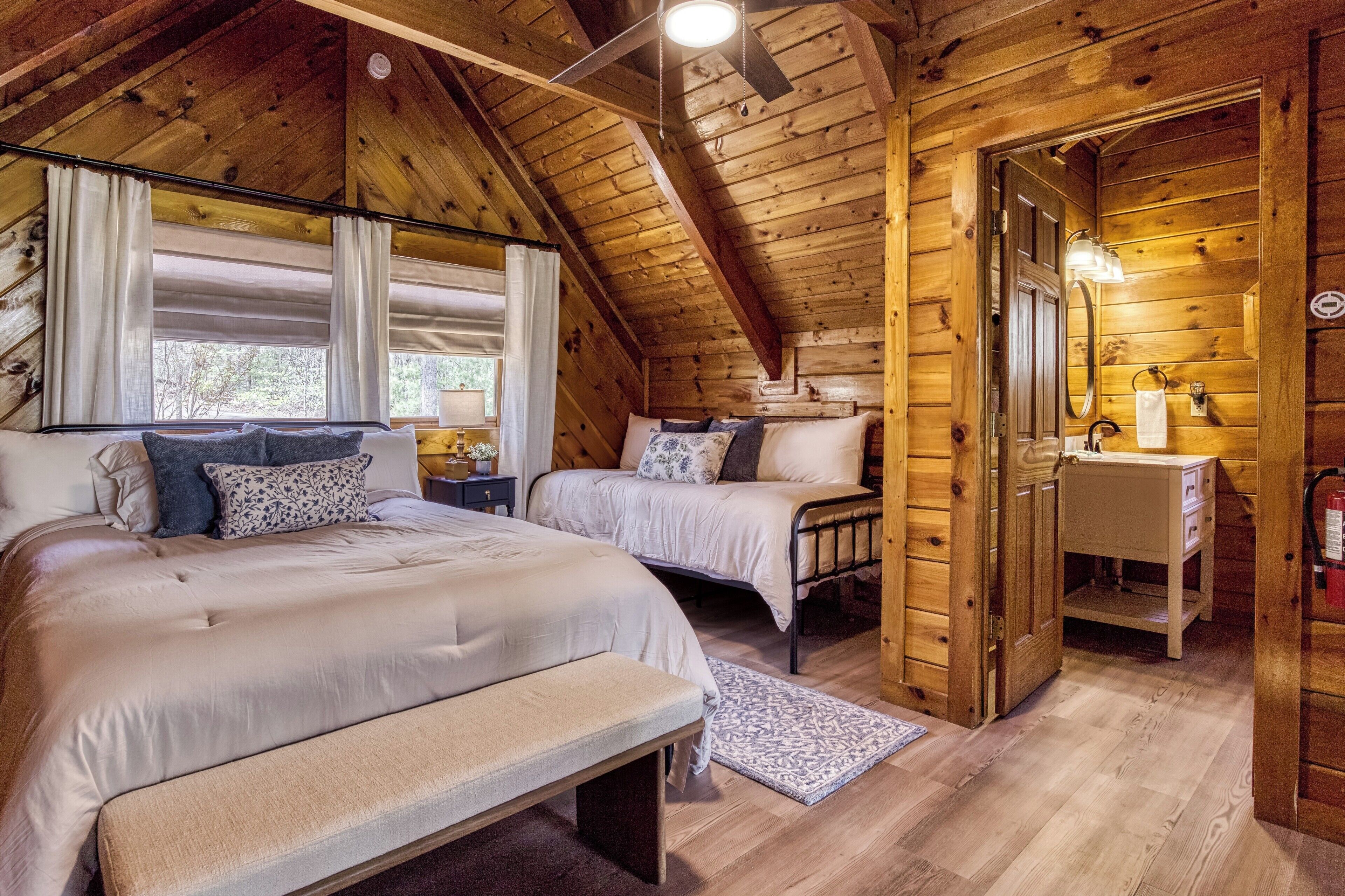 Une chambre dans une cabane en bois, avec deux lits, un banc, une table de chevet, une commode et un miroir.