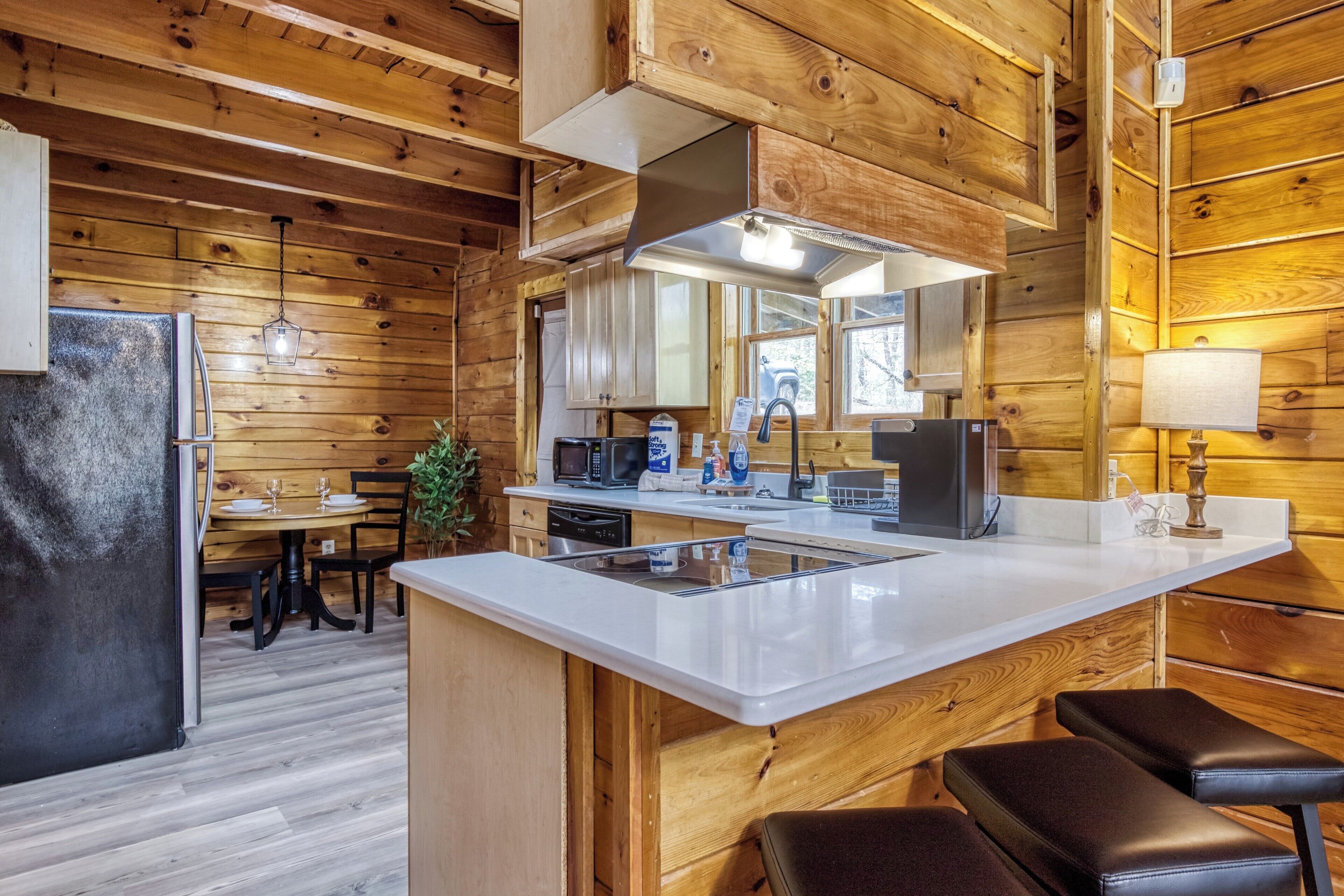 A wooden cabin interior with a kitchen, dining area, and bar seating.