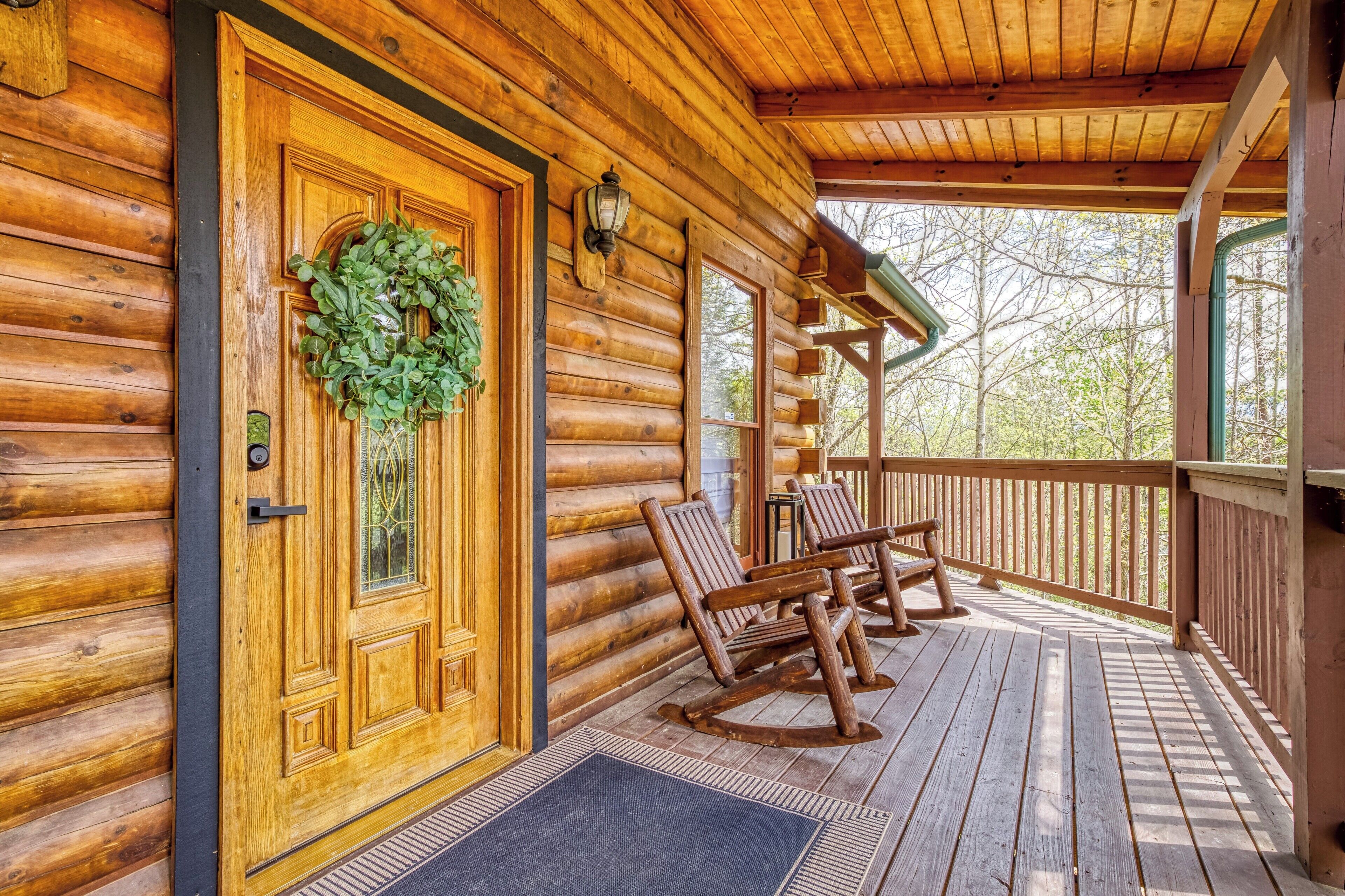 Une cabane en rondins avec une porte en bois, une couronne de Noël, des fauteuils à bascule et une véranda.