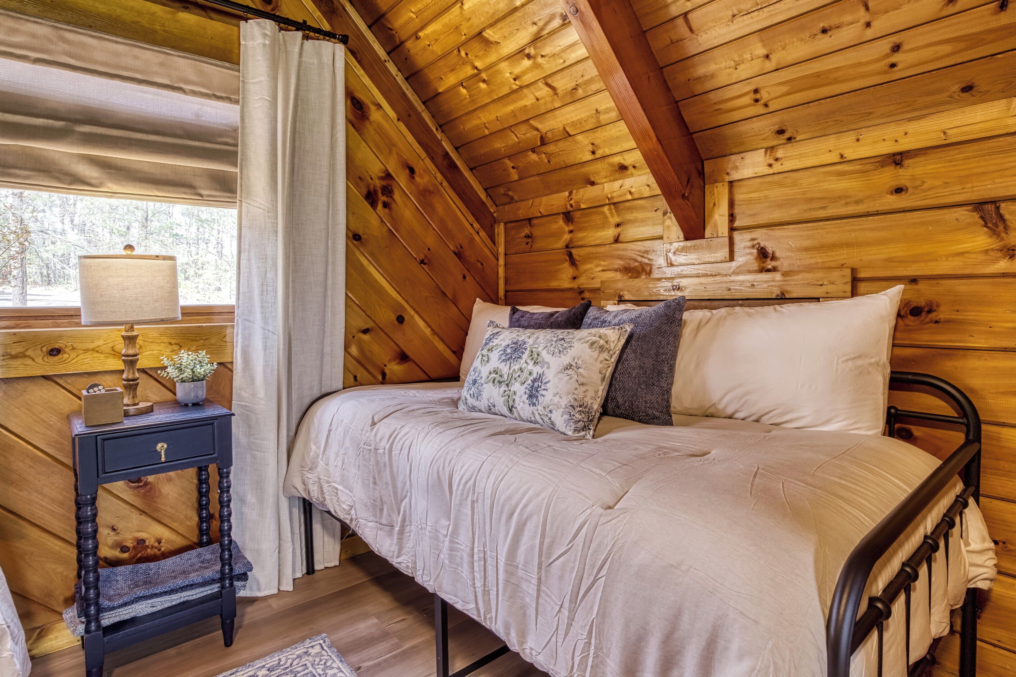 Une chambre à coucher dans un chalet en bois, avec un lit, une table de chevet, une lampe et une fenêtre avec des rideaux.