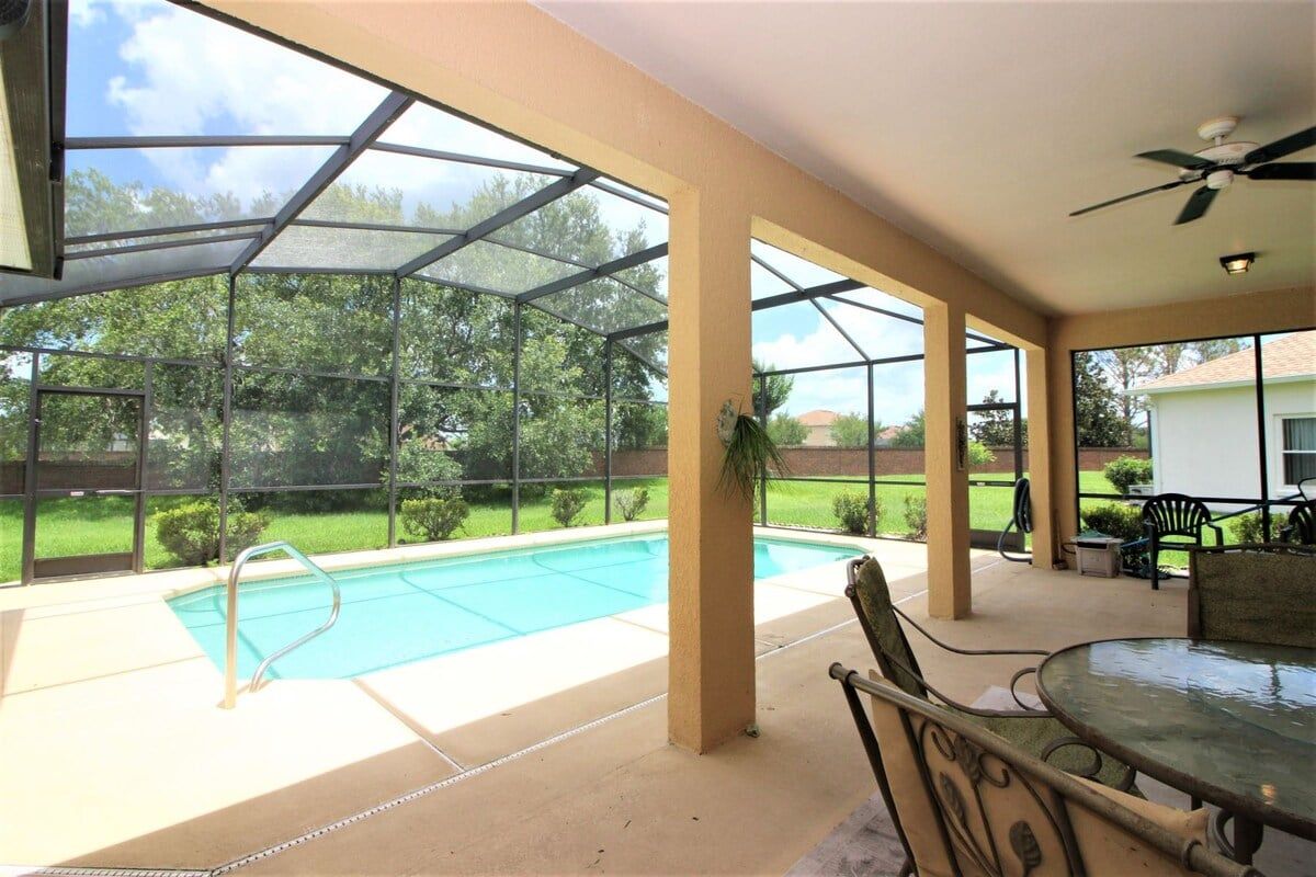 A covered outdoor area with a pool, patio furniture, and a view of a residential neighborhood.