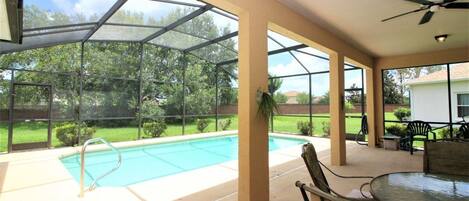 A covered outdoor area with a pool, patio furniture, and a view of a residential neighborhood.