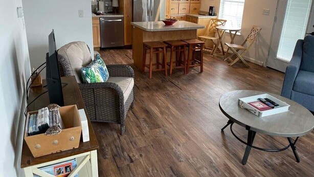 A modern living room with a large TV, a comfortable sofa, and a dining area with wooden chairs. - Peach on the Beach - 3BR/2 BA - Fort Morgan - Pet Friendly (Gulf Shores)