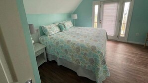 A bedroom with a bed, a nightstand, a lamp, and a window with blinds. - Peach on the Beach - 3BR/2 BA - Fort Morgan - Pet Friendly (Gulf Shores)