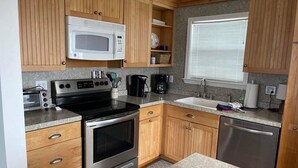 A compact kitchen with wooden cabinets, a microwave, a stove, a sink, and a dishwasher. - Peach on the Beach - 3BR/2 BA - Fort Morgan - Pet Friendly (Gulf Shores)