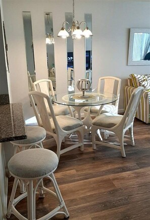 Een eetruimte met een glazen tafel, omringd door comfortabele stoelen, een hanglamp en een spiegel aan de muur.