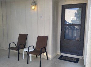 Een deur met daarboven het nummer '602', een deurmat en twee stoelen ervoor.