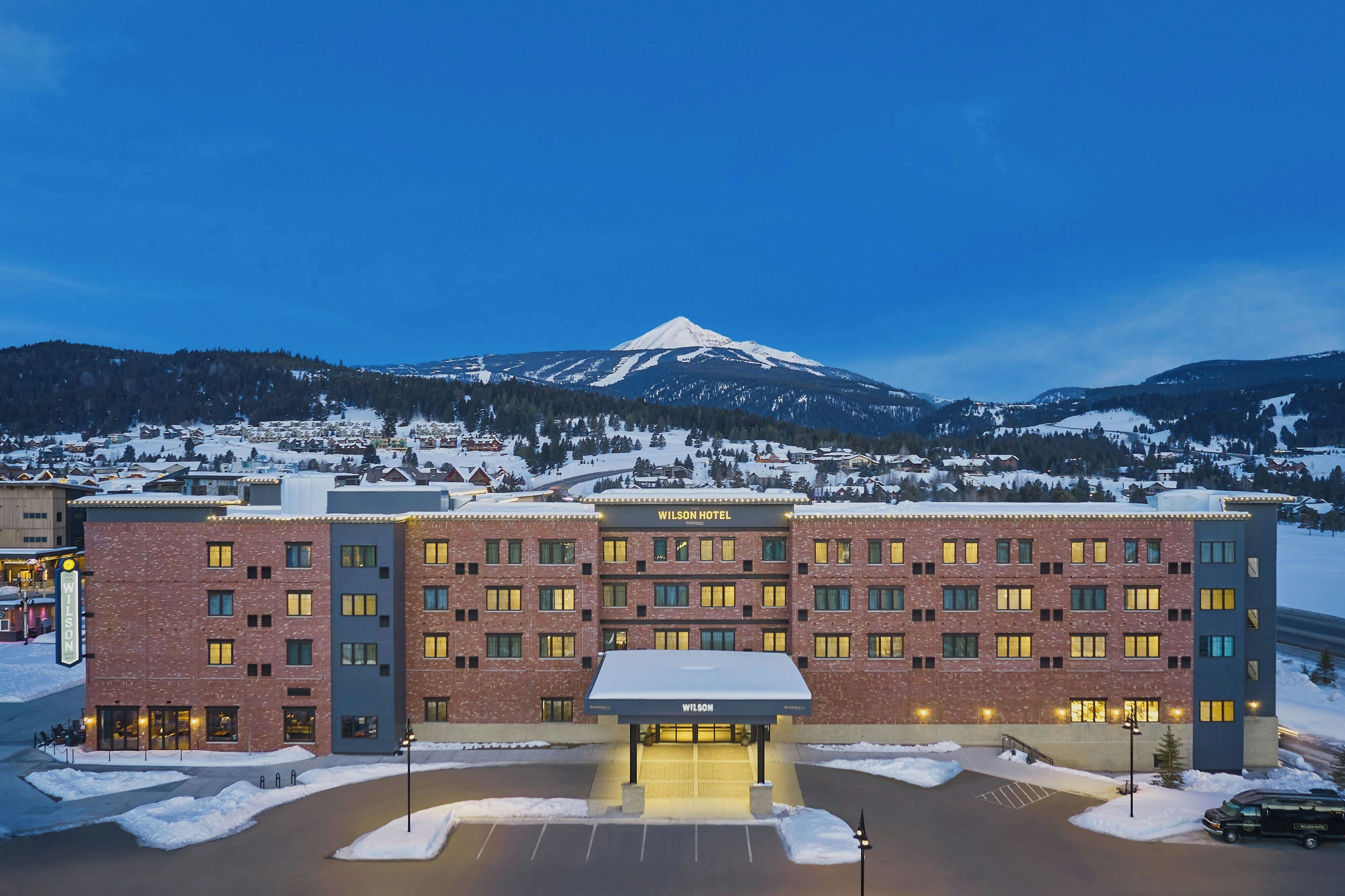A hotel with a prominent entrance, multiple floors, and a mountain in the background.