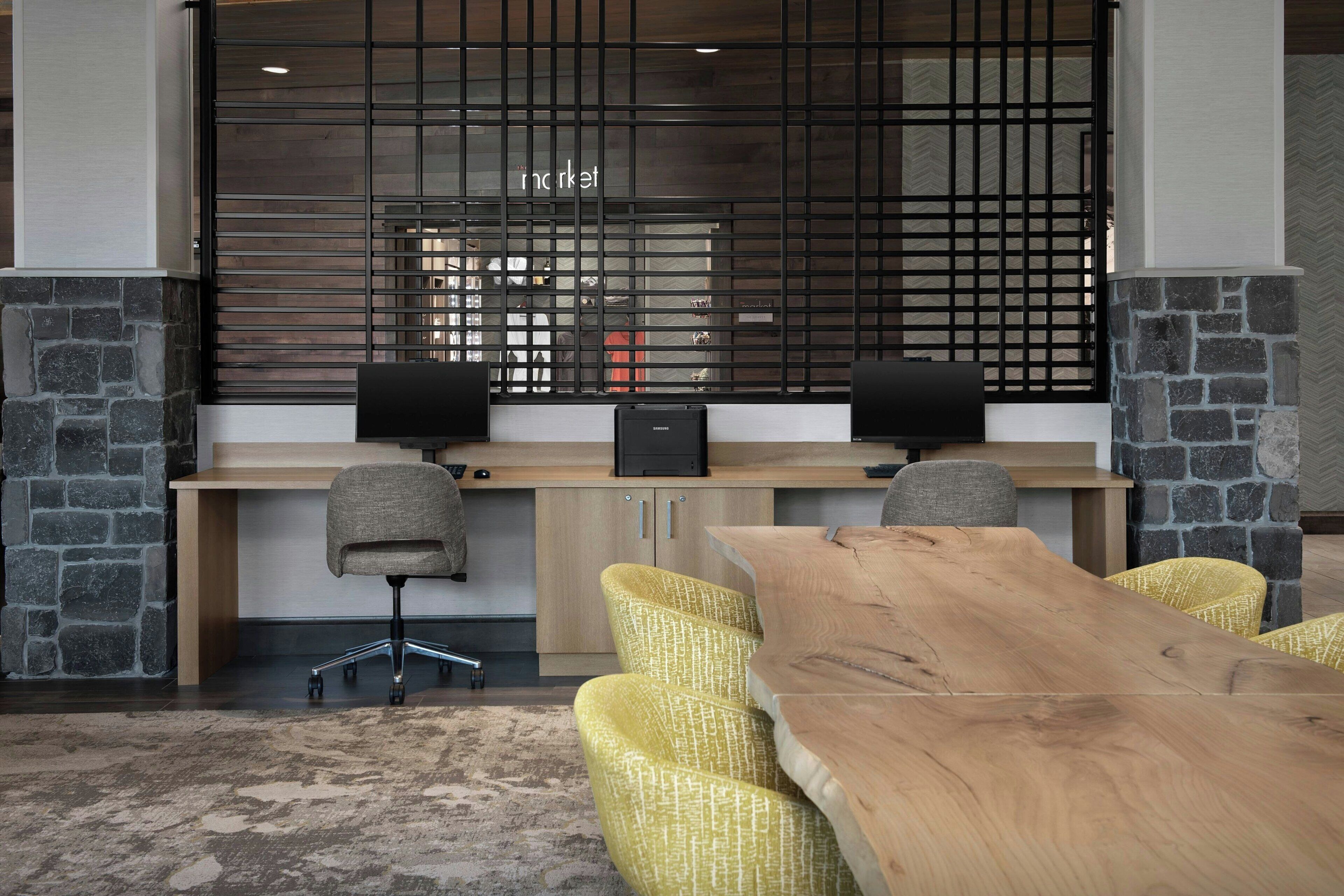A modern office space with a long wooden table, yellow chairs, a black desk with two speakers, and a stone accent wall.