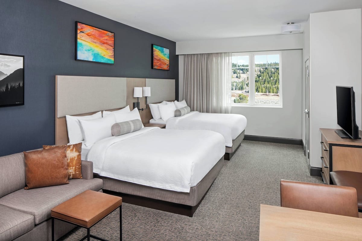 A hotel room with two beds, a sofa, a TV, and a window with a view.