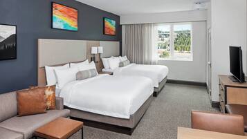 A hotel room with two beds, a sofa, a TV, and a window with a view.