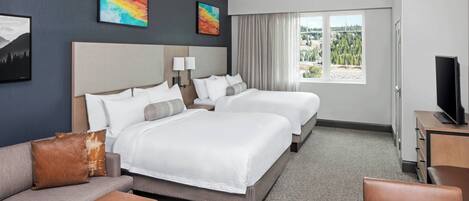A hotel room with two beds, a sofa, a TV, and a window with a view.