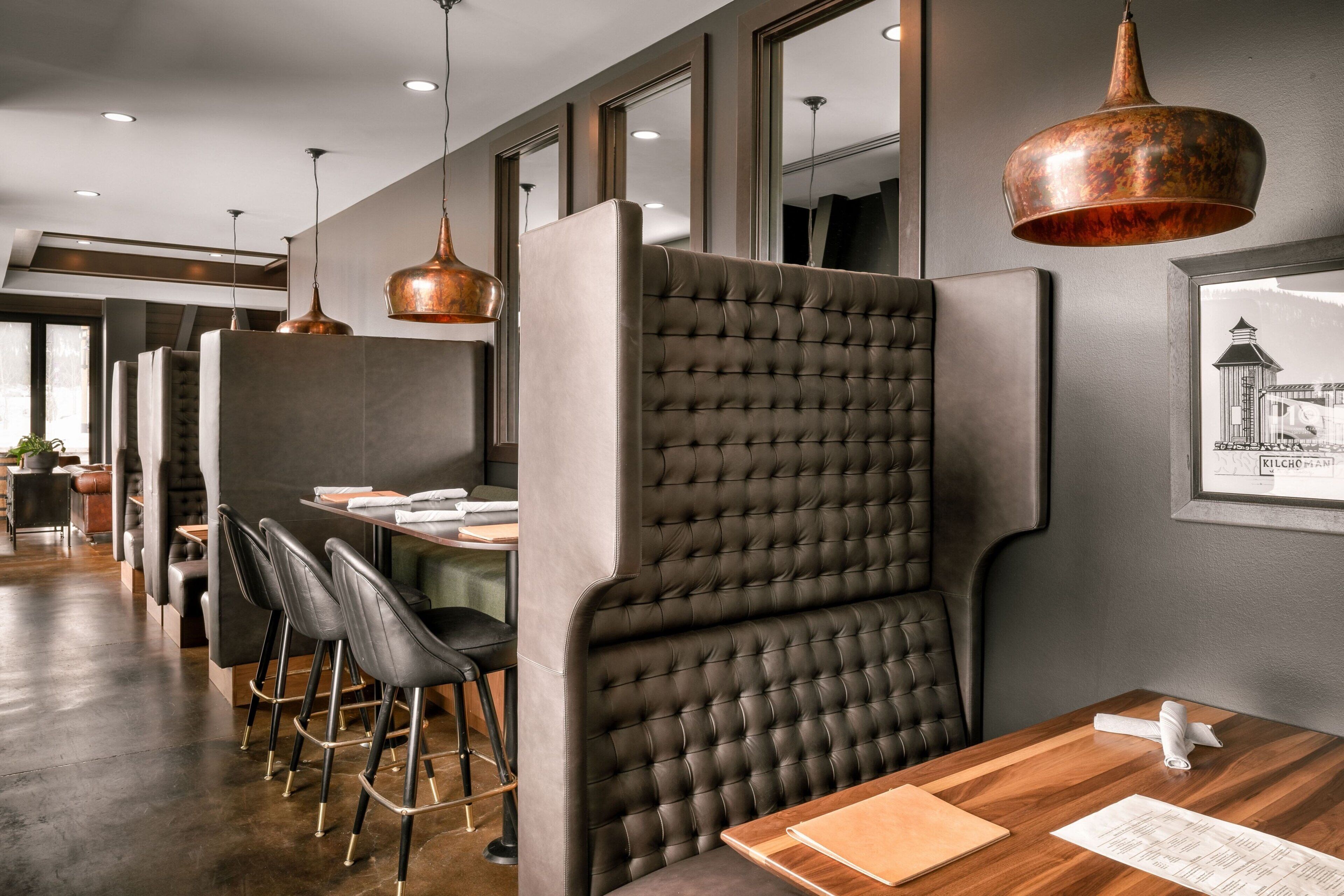 A modern restaurant with high-backed booths, copper pendant lighting, and a framed historical picture on the wall.