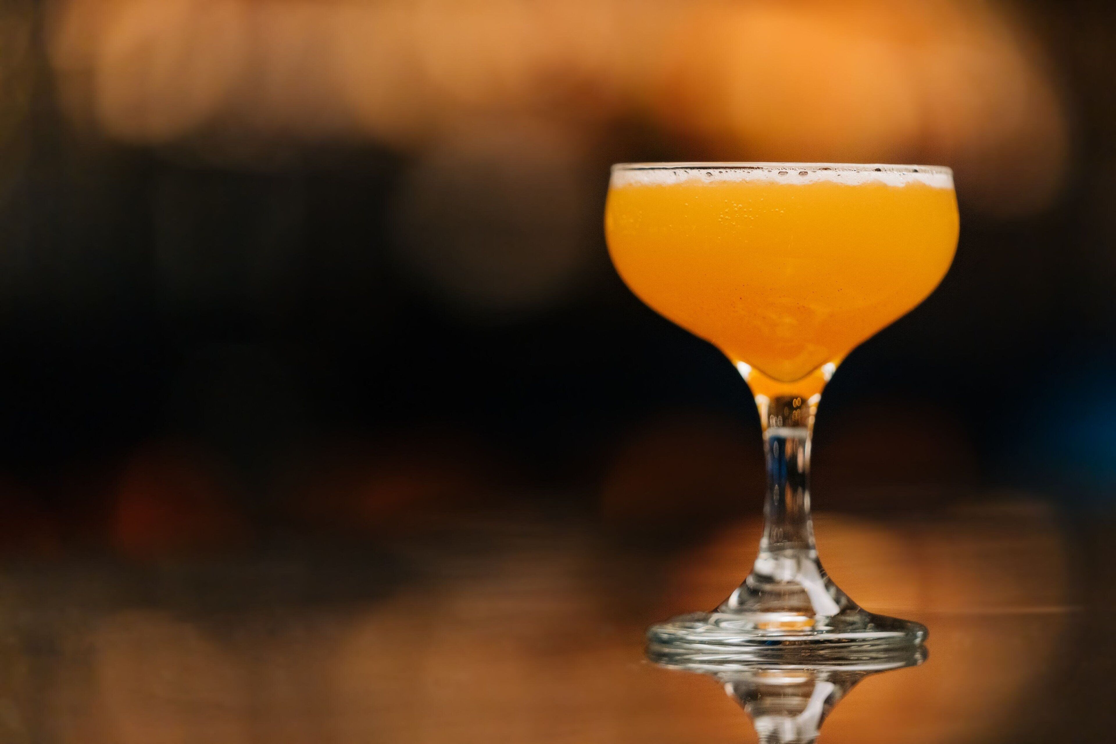 Un vaso de jugo de naranja transparente sobre una superficie reflectante.