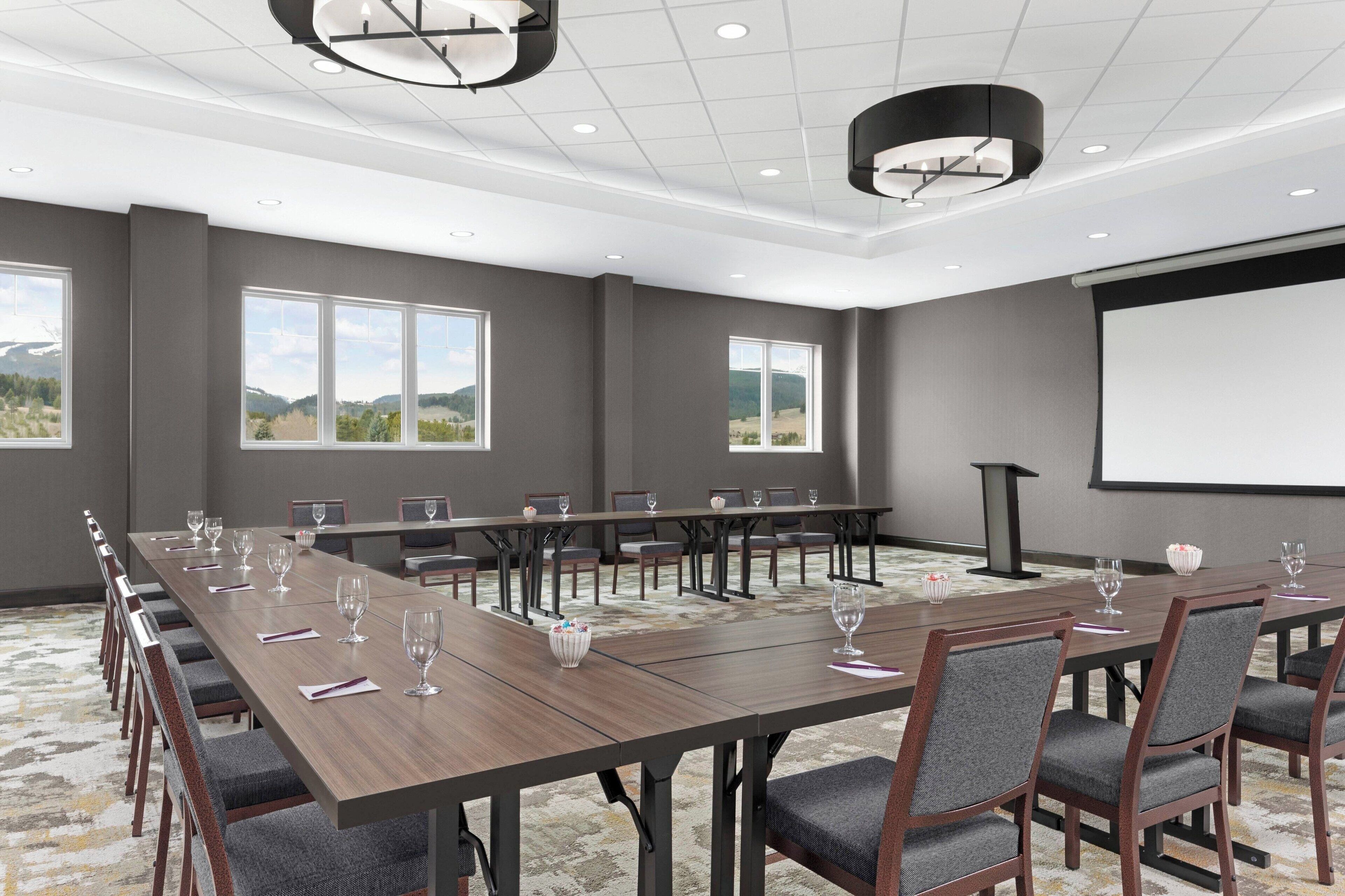 A conference room with long tables, chairs, and a projector screen.
