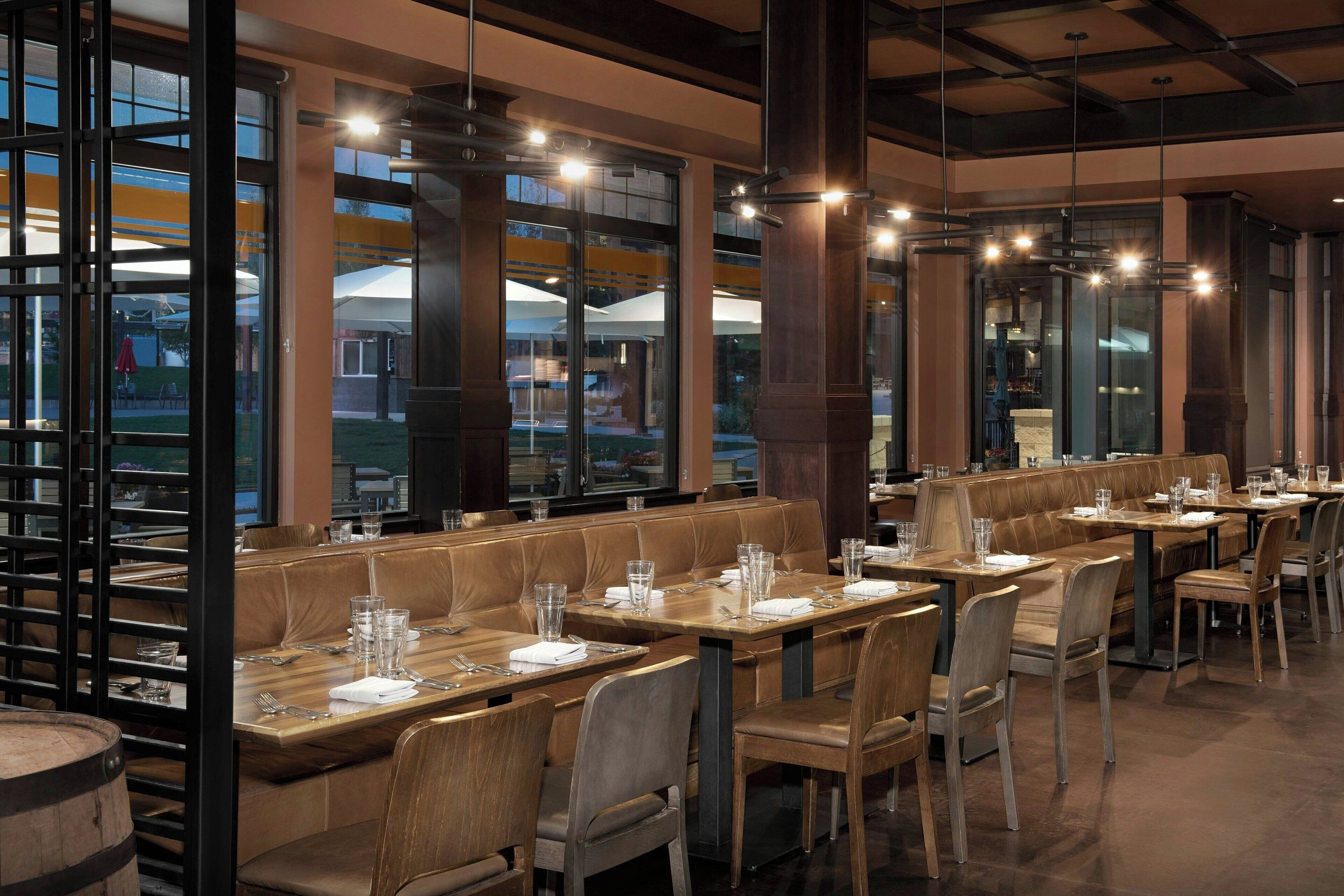 A restaurant with booth seating, wooden tables, and hanging pendant lights.