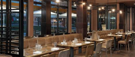 A restaurant with booth seating, wooden tables, and hanging pendant lights.