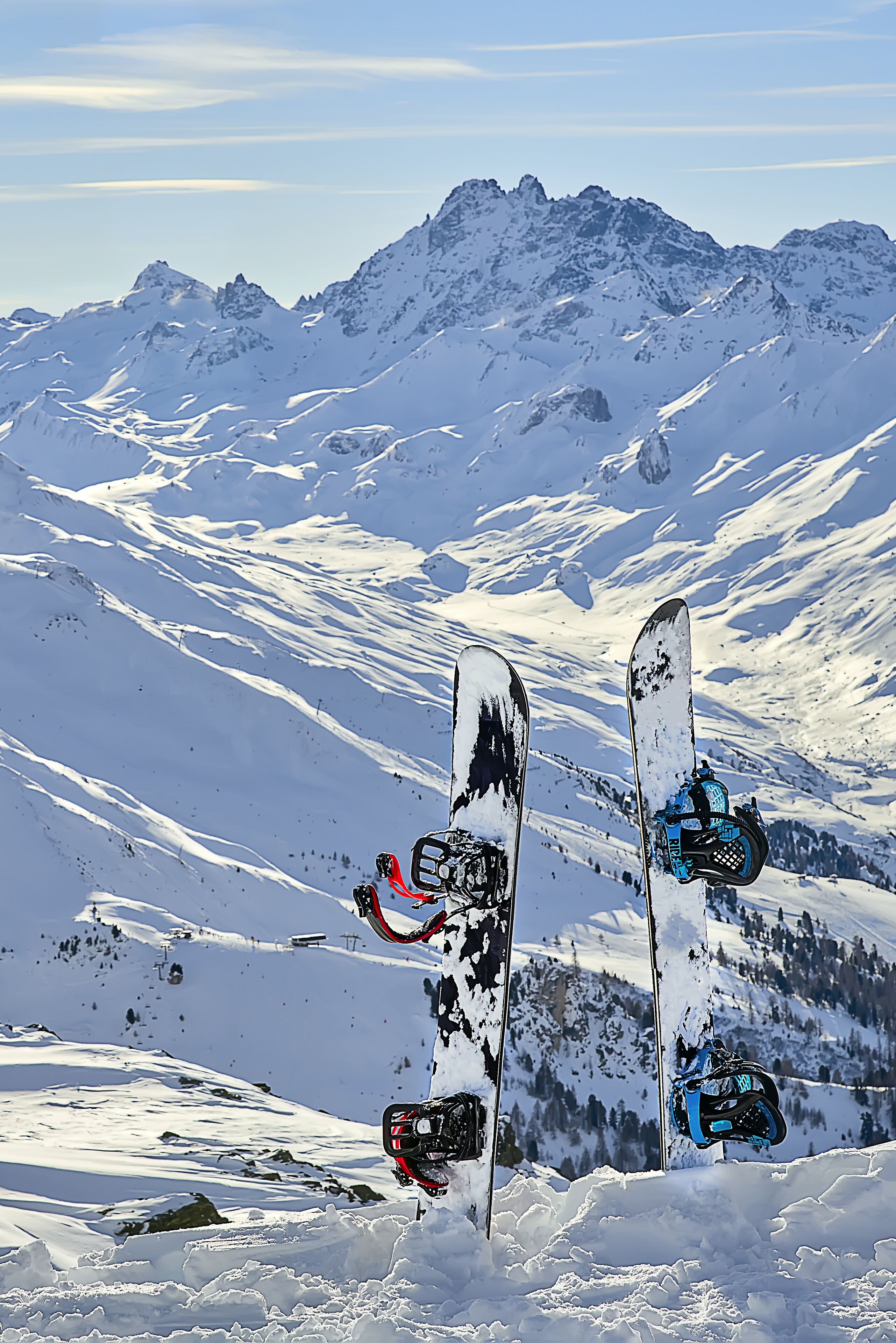 Zwei Snowboards lehnen an einem verschneiten Berghang, mit blauem Himmel und fernen Berggipfeln.