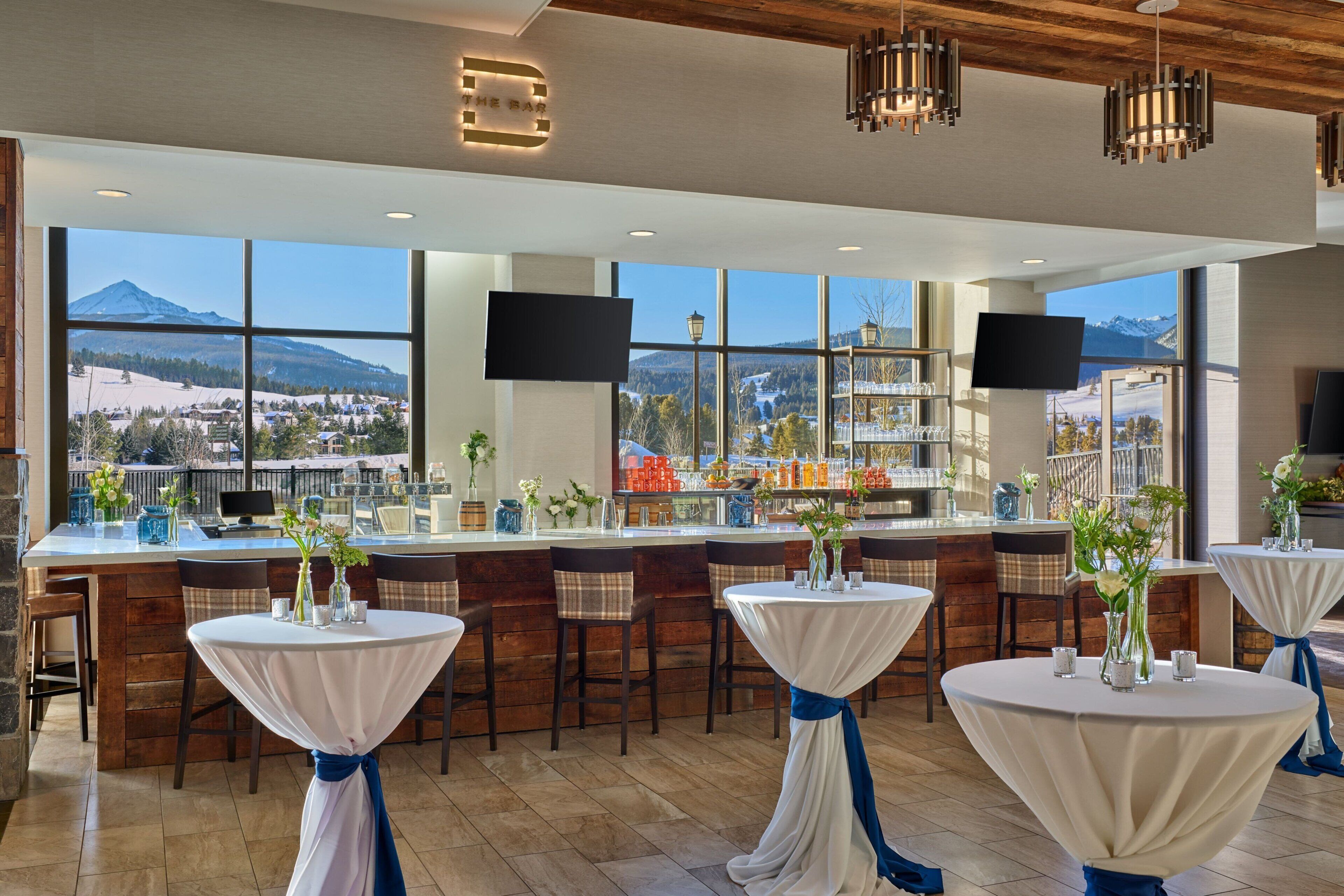 Un restaurante con zona de bar, amplios ventanales y vistas a la montaña, con una decoración de diseño moderno.