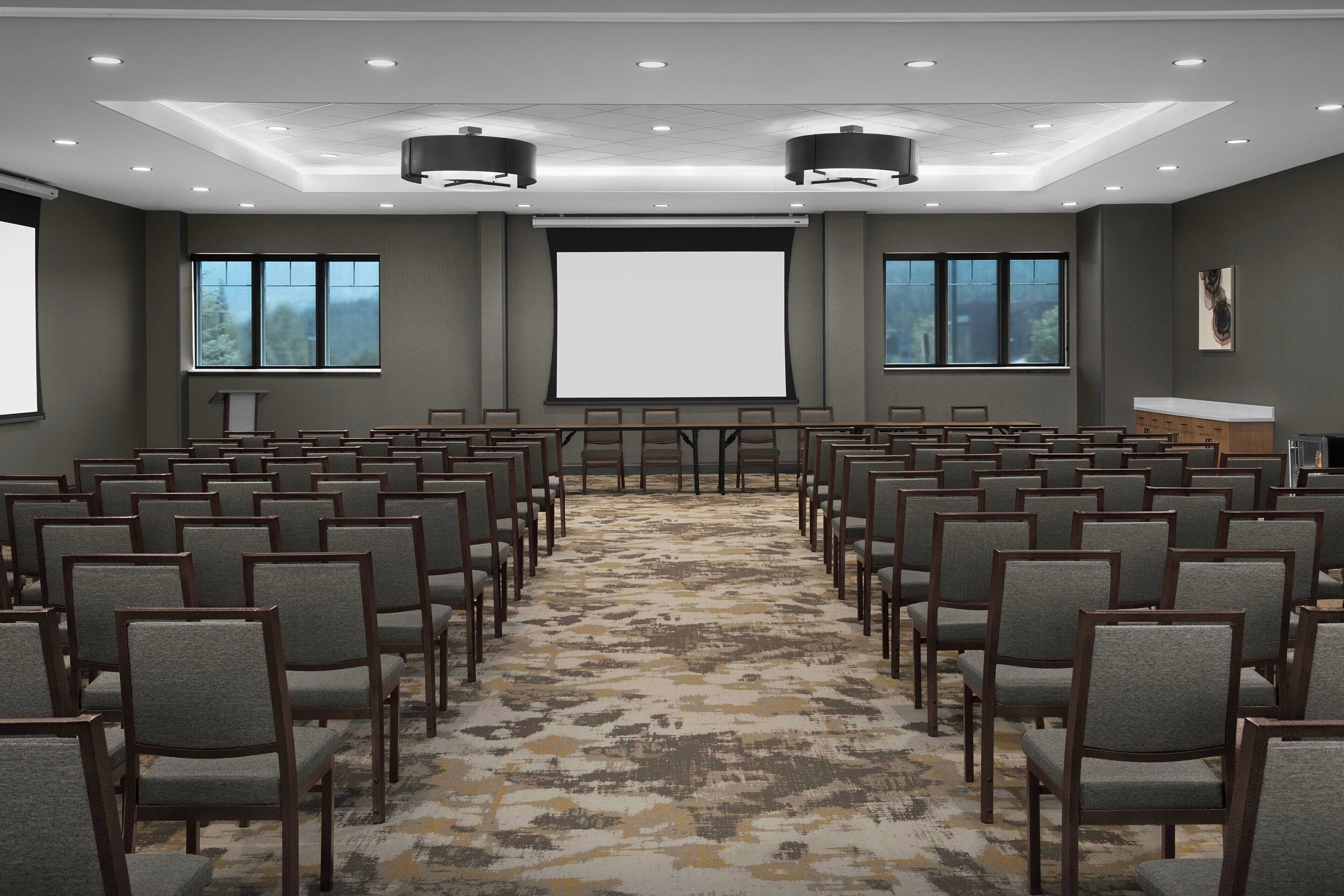 A conference room with rows of chairs, a large screen, and a podium.