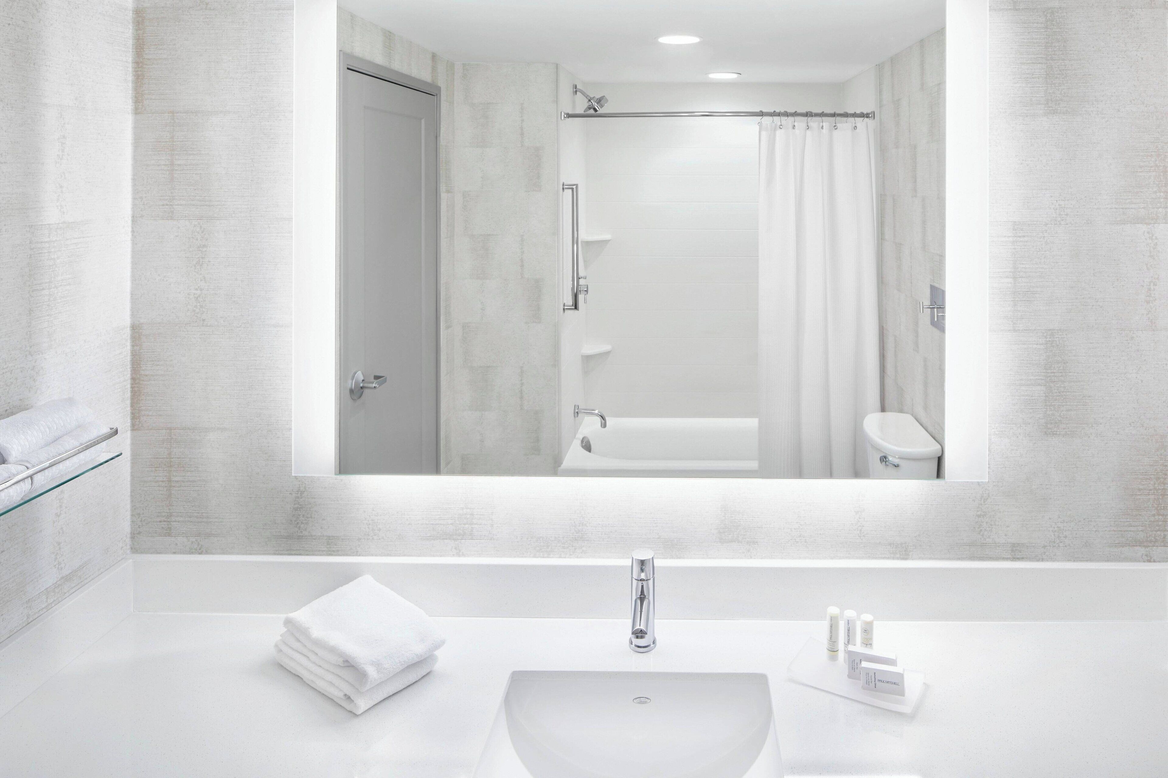A modern bathroom with a large mirror, a white sink, and a shower.